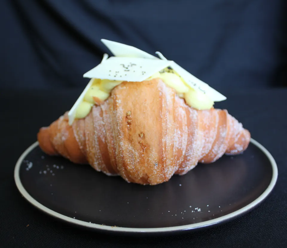 Croissant con crema clara y láminas de chocolate blanco encima, en un plato negro