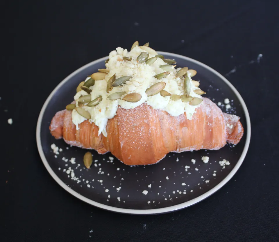 Croissant con crema blanca y pepitas encima, en un plato negro