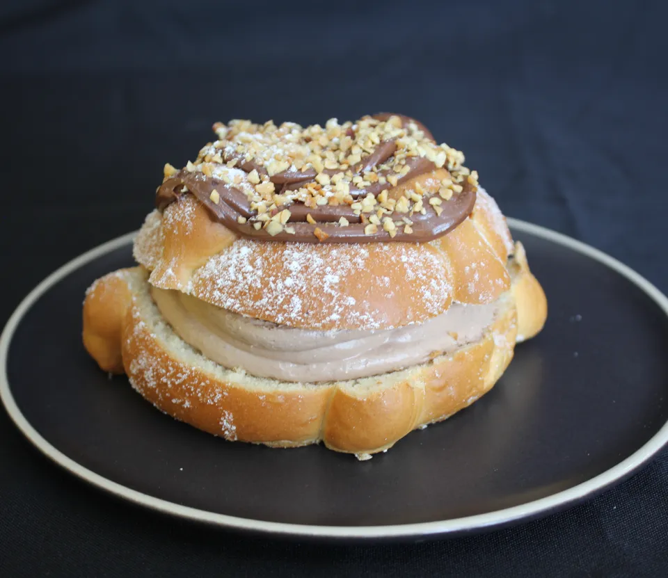 Pan de muerto relleno de crema de chocolate, con Nutella y trocitos encima, en un plato negro